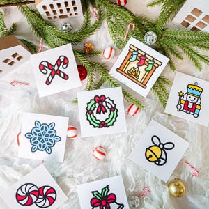 May include: A collection of eight square white cards featuring colorful Christmas illustrations including candy canes, a fireplace with stockings, a nutcracker, a snowflake, a wreath, a bell, peppermint candies, and two bells with a red bow.