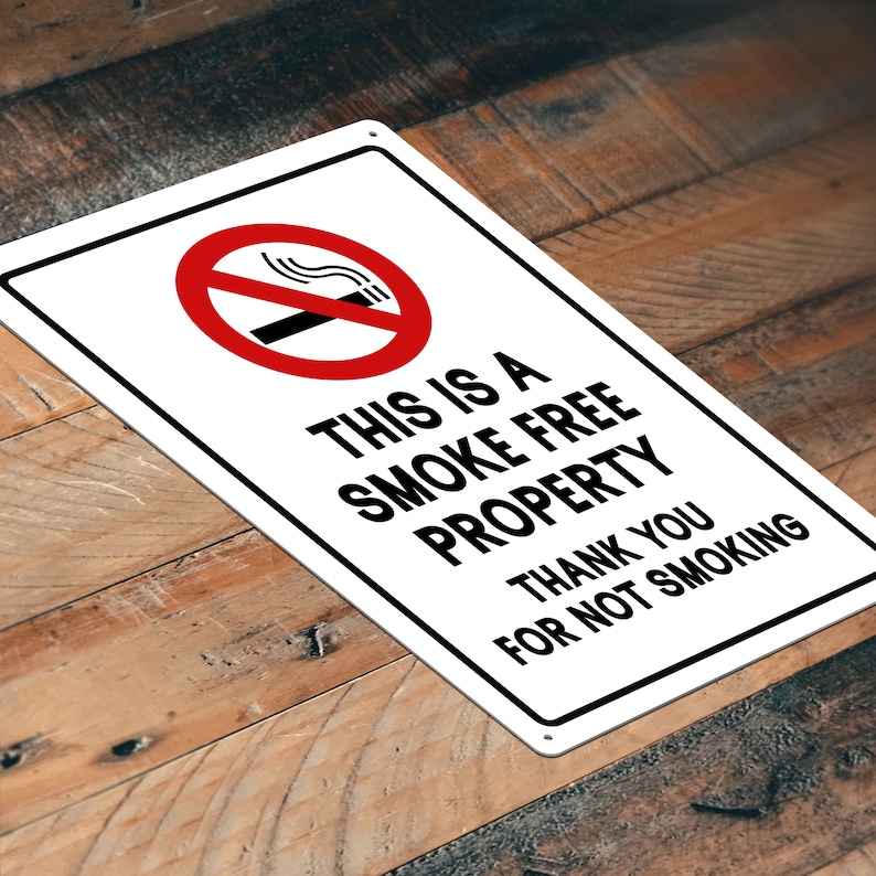 Puede incluir: Un letrero de metal blanco con un c&iacute;rculo rojo y una l&iacute;nea diagonal que atraviesa un cigarrillo con humo. El letrero dice "Esta es una propiedad libre de humo. Gracias por no fumar."