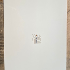 Puede incluir: Un letrero de metal blanco con esquinas redondeadas y cuatro agujeros para colgar. El letrero tiene un peque&ntilde;o logotipo gris en el centro que dice "JP's Parcels".