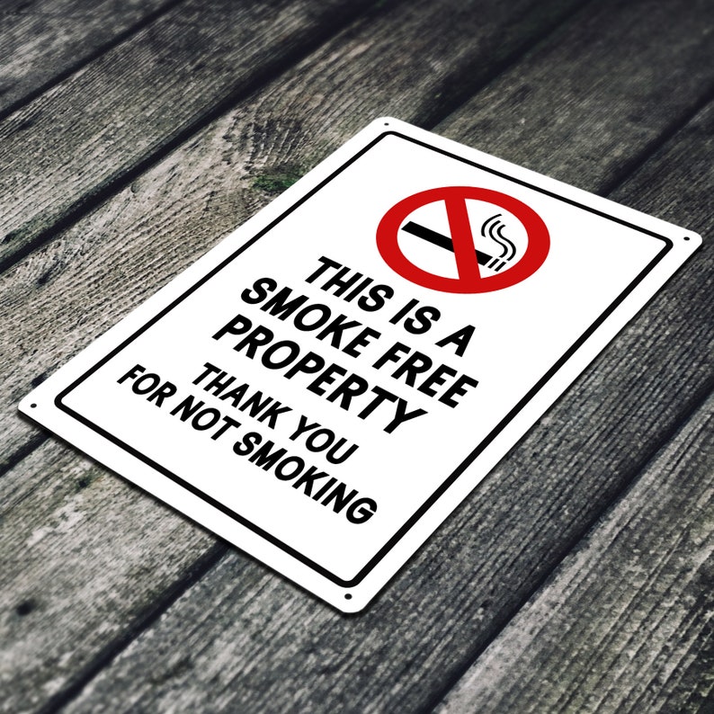 Puede incluir: Un letrero de metal blanco con texto negro que dice "This is a smoke free property. Thank you for not smoking." Un c&iacute;rculo rojo con una l&iacute;nea diagonal que lo atraviesa y un cigarrillo con humo saliendo de &eacute;l se encuentra en la esquina superior izquierda.