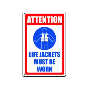 May include: Red and white sign with the words "ATTENTION" in large white letters. A blue circle with a white stick figure wearing a life jacket is in the center. The words "LIFE JACKETS MUST BE WORN" are below the circle.