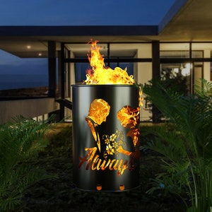 Può includere: Un braciere in metallo nero con un designo a taglio di una coppia che si tiene per mano e la parola "Always". Il braciere sta bruciando con fiamme arancioni.
