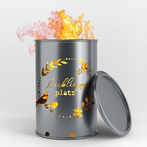 Può includere: Un braciere in metallo grigio con un design a taglio di un uccello, foglie e cuori. Il braciere ha il testo "Lieblingsplatz" su di esso. Il braciere è acceso e ha fiamme che escono dalla parte superiore.