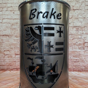 Può includere: Un braciere in metallo argentato con un designo a taglio di uno stemma che presenta una nave, un uccello e una croce. Il braciere ha la scritta "Brake" in cima.