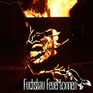 Può includere: Un focolare in metallo con la silhouette di una strega e una volpe. Il focolare è acceso e le fiamme sono visibili attraverso i ritagli. Il testo "Fuchsbau Feuertönnen" è visibile nella parte inferiore dell'immagine.