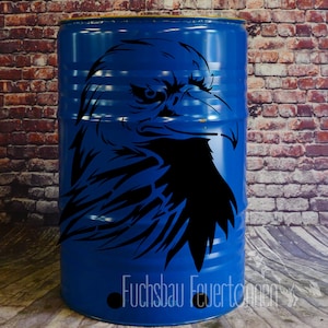 Può includere: Un barile di metallo blu con un design a silhouette di aquila nera. Il barile ha il testo "Fuchsbau Feuertonnen" stampato sul fondo.