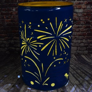 Può includere: Un cilindro di metallo blu con la parte superiore gialla, che presenta un design ritagliato di fuochi d'artificio in giallo. Il cilindro è un pezzo decorativo dall'aspetto rustico.