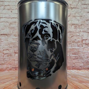 Può includere: Un braciere in metallo argentato con una silhouette nera di una testa di cane ritagliata. Il braciere ha un coperchio e diversi fori intorno alla parte inferiore.