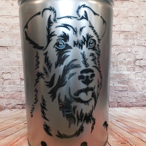 Può includere: Un braciere in metallo argentato con una silhouette nera di una testa di cane ritagliata. Il braciere ha un coperchio con una maniglia.