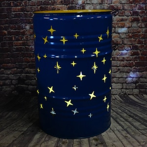 Può includere: Un barile di metallo blu con un top giallo e stelle ritagliate. Il barile è dipinto di blu scuro e ha un bordo giallo attorno al top. Le stelle sono ritagliate nel metallo e sono di una tonalità di giallo più chiara.