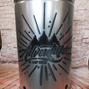 Può includere: Un contenitore in metallo argentato con un design grafico nero che presenta una catena montuosa e il testo "Adventure is out there".