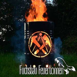 Può includere: Un focolare in metallo nero a forma di barile con un design ritagliato di due martelli incrociati all'interno di un cerchio. Il focolare sta bruciando con fiamme arancioni e fumo. Il testo "Fuchsbau Feuertönnen" è visibile nella parte inferiore dell'immagine.