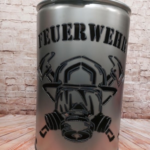 Può includere: Un braciere in metallo argentato con un designo a taglio nero di un casco da pompiere e una maschera antigas. Il testo "FEUERWEHR" è tagliato sulla parte anteriore del braciere.