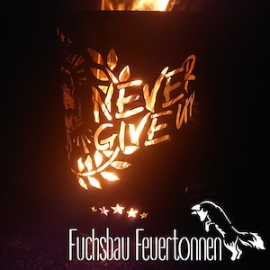 Può includere: Un braciere in metallo nero con un design a taglio delle parole "Never Give Up" e un design di ramo frondoso. Il braciere è acceso e brilla di colore arancione. Il testo "Fuchsbau Feuertönnen" è visibile nella parte inferiore dell'immagine.
