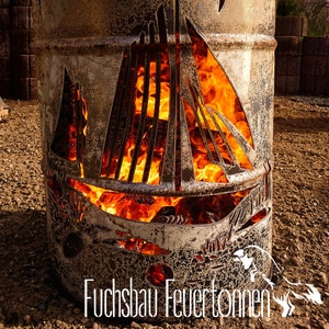 Può includere: Un focolare in metallo a forma di nave con fiamme che bruciano all'interno. Il focolare è realizzato con un barile di metallo riutilizzato e ha un aspetto rustico e invecchiato. Il testo "Fuchsbau Feuertonnen" è visibile nella parte inferiore dell'immagine.