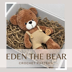 May include: A handmade crochet teddy bear in a gift box. The bear is brown with a white muzzle and wears tan overalls. The box contains brown paper filler. The text "EDEN THE BEAR CROCHET PATTERN" is visible.