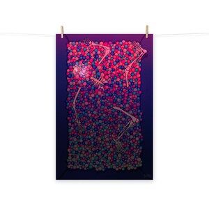 Pode incluir: Uma impressão em pôster que retrata um esqueleto submerso em um mar de bolas coloridas. A obra de arte apresenta um fundo azul escuro com os ossos do esqueleto e as bolas em tons de rosa, azul e roxo. A impressão é presa por clipes de madeira em uma corda branca.