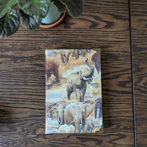 Peut inclure: Un carnet brun et beige avec une couverture représentant un motif d'éléphants dans un décor de safari.