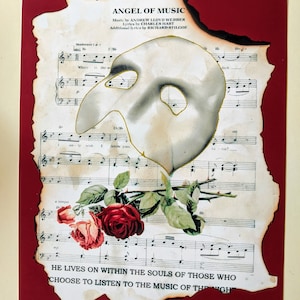 May include: A vintage sheet music page with a burnt edge, featuring the song "Angel of Music" from the musical "The Phantom of the Opera". The sheet music includes lyrics and musical notation. A white mask with gold accents is superimposed on the page, and red roses are placed at the bottom.