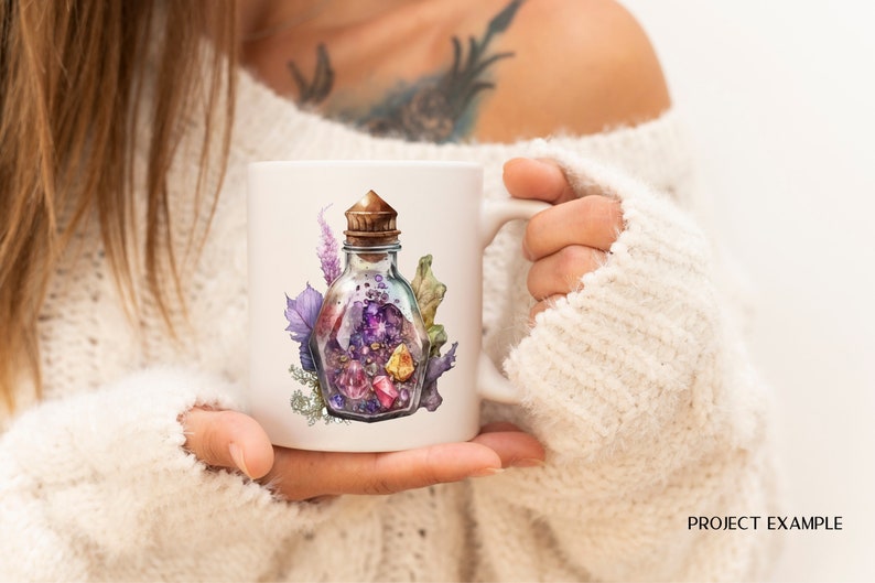 Peut inclure: Mug en c&eacute;ramique blanche avec une illustration &agrave; l'aquarelle d'une bouteille en verre remplie de cristaux color&eacute;s et d'un bouchon en li&egrave;ge. La bouteille est entour&eacute;e de feuillage violet et vert. Le mug est tenu par une personne portant un pull blanc.