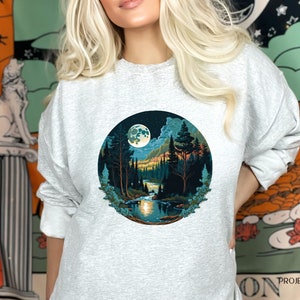 May include: A gray sweatshirt with a circular graphic of a moonlit forest scene. The graphic features a full moon, trees, a river, and mountains in shades of blue, green, and orange.