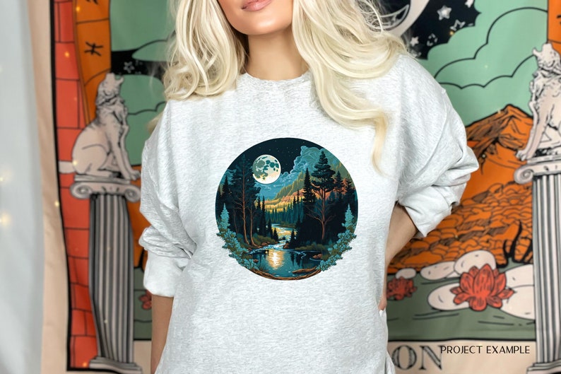 May include: A gray sweatshirt with a circular graphic of a moonlit forest scene. The graphic features a full moon, trees, a river, and mountains in shades of blue, green, and orange.