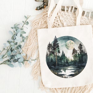 May include: A white canvas tote bag with a circular design featuring a watercolor painting of a moonlit forest scene. The scene includes a lake, trees, and a full moon.