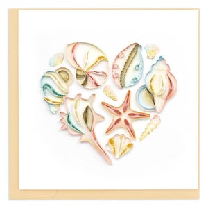 May include: A greeting card featuring a heart-shaped arrangement of paper quilled seashells and a starfish in shades of pink, white, and yellow. The card is on a white background with a cream-colored border.