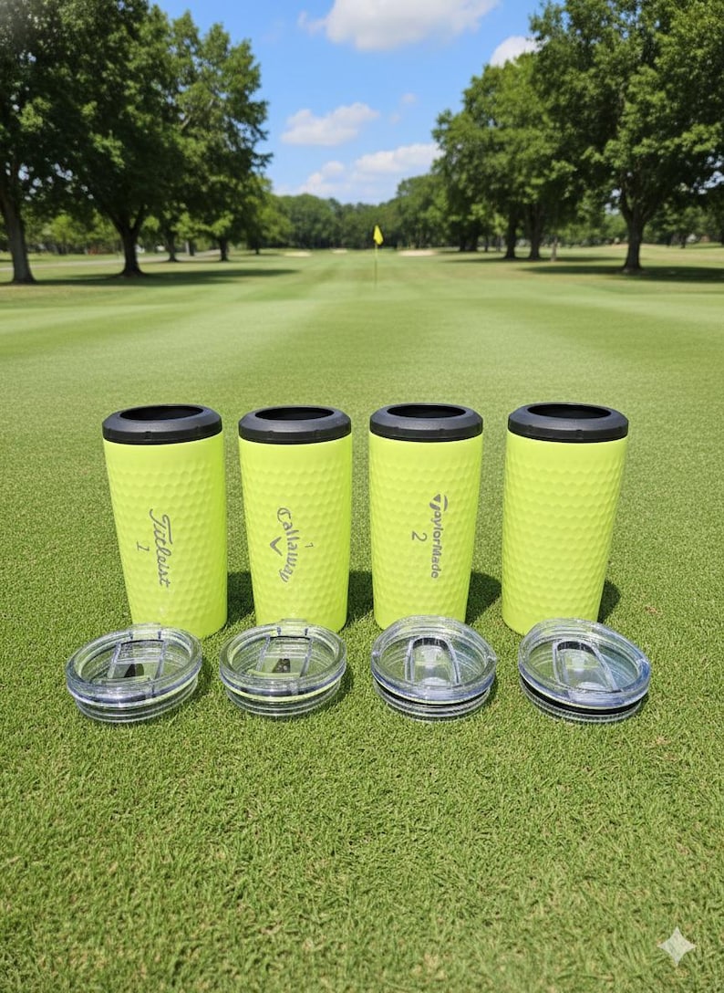 May include: Four neon green golf ball textured tumblers with black rims and clear lids are displayed on a golf course. The tumblers have the logos of golf brands Titleist, Callaway, and TaylorMade. The background shows a green golf course.