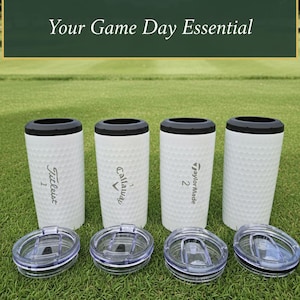 May include: Four white golf ball textured tumblers with black rims and clear lids are displayed on green grass. The tumblers have the logos of golf brands Titleist, Callaway, and TaylorMade. The text "4-in-1 Golf Tumbler!" and "Your Game Day Essential" are at the top.