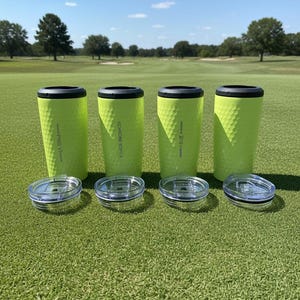 May include: Four lime green insulated tumblers with black rims and clear lids are arranged on a golf course. The tumblers have a textured surface and the text "PRO V1", "4 CHROME SOFT", and "T-5" are printed on them.