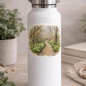 May include: White water bottle with a silver handle and lid. The bottle features a sticker with a watercolor painting of a wooden boardwalk winding through a forest with lush green ferns and trees.