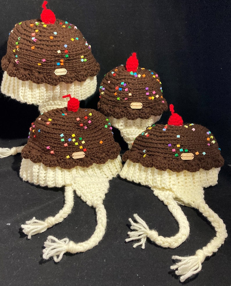 May include: Three crocheted ice cream cone hats with white yarn and brown yarn for the ice cream. The hats have colourful sprinkles and a red cherry on top. Each hat has a brown tag that says "Handmade".