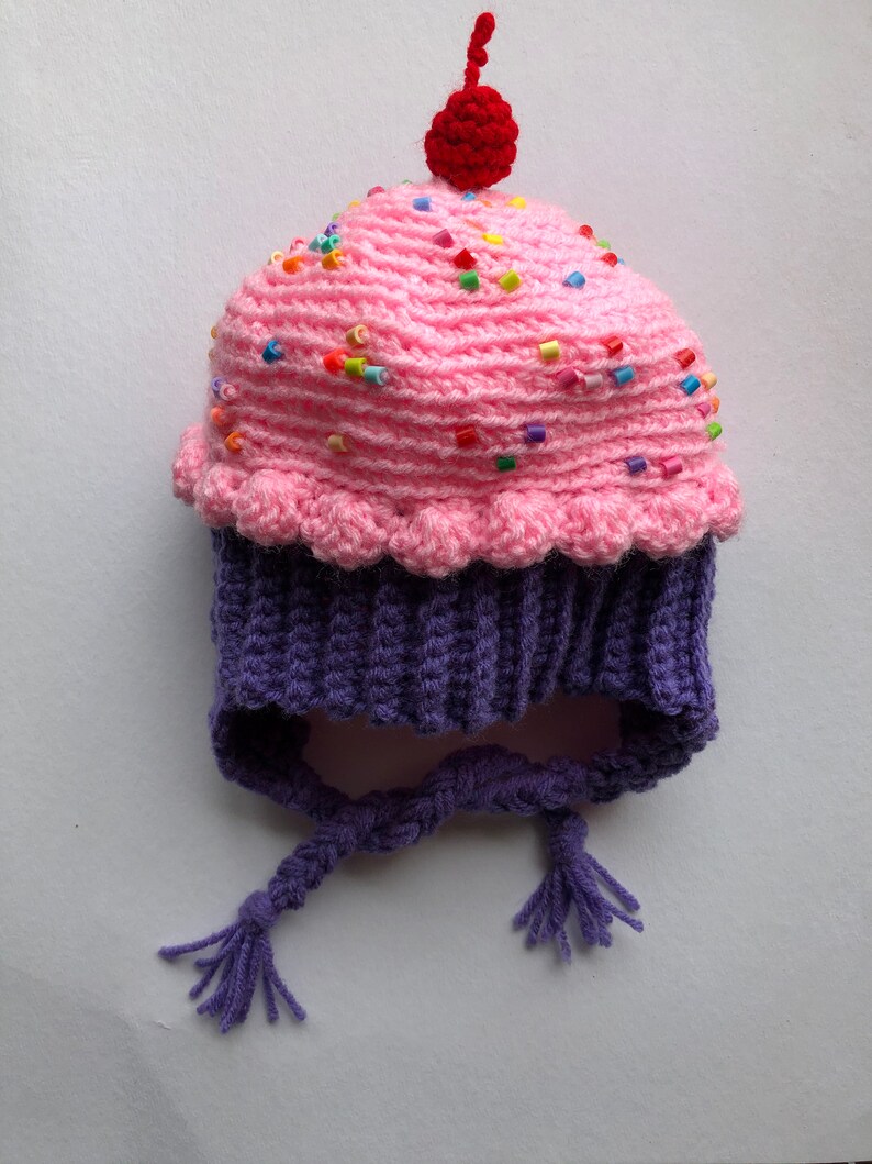 Puede incluir: Un gorro de cupcake tejido a crochet, rosa con cuentas de colores y una cereza roja. La base es morada con lazos trenzados. Un accesorio divertido y hecho a mano para ni&ntilde;os, ideal para disfraces.