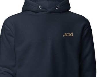 May include: Navy blue hoodie with a kangaroo pocket and drawstring hood. The word ",and" is embroidered in gold thread on the upper chest. A casual, comfortable garment for everyday wear.