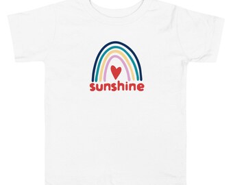 Może przedstawiać: Biała koszulka dla małych dzieci z grafiką tęczy i napisem "sunshine" czerwonymi literami. W środku tęczy znajduje się czerwone serce.
