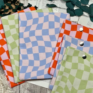 Könnte beinhalten: Eine Sammlung farbenfroher Stoffbeutel mit einem wellenförmigen Schachbrettmuster. Die Beutel haben Farben wie Orange, Rosa, Hellblau und Grün. Jeder Beutel hat einen silbernen Druckknopfverschluss.