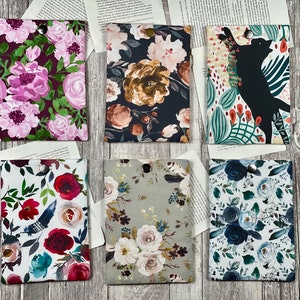 Può includere: Sei diverse cover in tessuto con motivi floreali per dispositivi elettronici. Le cover sono tutte rettangolari e hanno una chiusura a bottone. I motivi includono fiori rosa e viola su sfondo scuro, fiori marroni e dorati su sfondo nero, fiori verdi e rossi su sfondo bianco, fiori rossi e bianchi su sfondo bianco, fiori bianchi e dorati su sfondo grigio e fiori blu e bianchi su sfondo bianco.