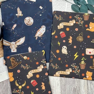 May include: Three fabric pouches with a magical theme. The pouches are black with a white and gold pattern of owls, stars, wands, and the word "MAGIC". The pouches are on a wooden surface.