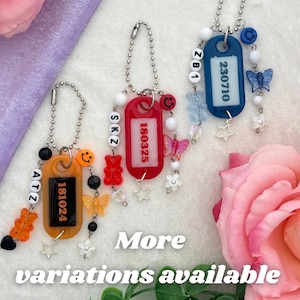 May include: Three beaded keychains on silver ball chains. The orange one features the text ATZ and 181024, the red one features SKZ and 180325, and the blue one features ZB1 and 230710. Each includes colorful beads, butterfly charms, and stars.