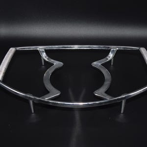 May include: A silver-colored metal trivet with a curved design. The trivet has two handles with a coiled texture and four small legs. The center features a stylized, wavy design.