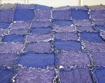 May include: A patchwork quilt made from various shades of blue and purple fabric. The quilt is made of squares and has a frayed edge.