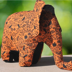 May include: Orange and black Halloween elephant plush toy with a black and white floral pattern. The elephant has a long trunk and large ears.