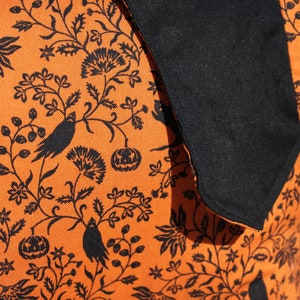 May include: Orange fabric with a black and white Halloween-themed print. The print features bats, pumpkins, and floral designs.
