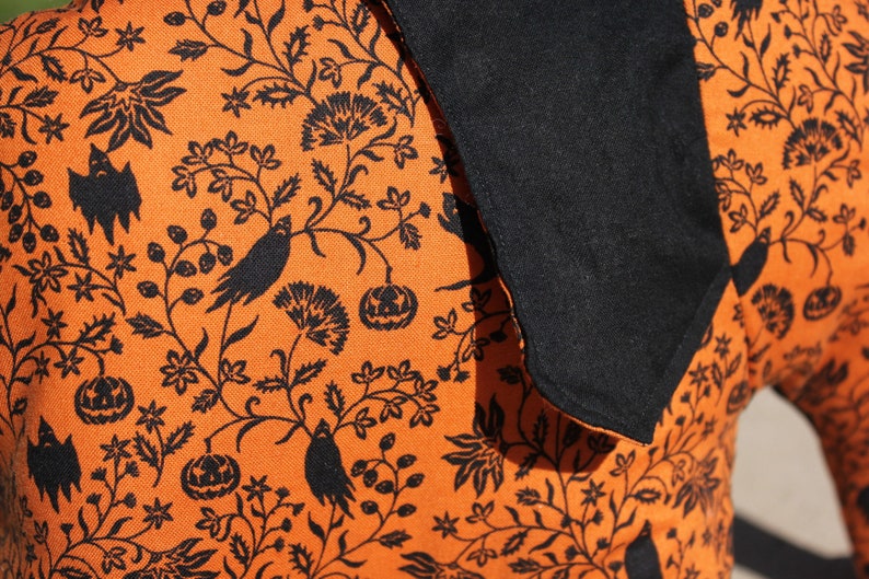 May include: Orange fabric with a black and white Halloween-themed print. The print features bats, pumpkins, and floral designs.