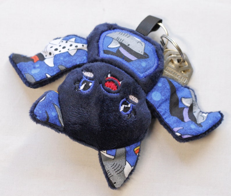 This bat plushie is 4 1/2' tall and 6 1/2' wide from wing to wing. It is made from dark blue minky fabric and a cotton fabric with sharks in Halloween costumes on it for the ears, wings, and belly. The belly is outlined in blue thread as well as the eyes. It has small white fangs and pink cheeks embroidered on its face. As well as a red mouth and red heart shaped nose.

Keys not included.