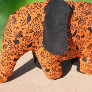 May include: Orange and black fabric elephant with a Halloween-themed print. The print features black bats, birds, and pumpkins on a repeating pattern.