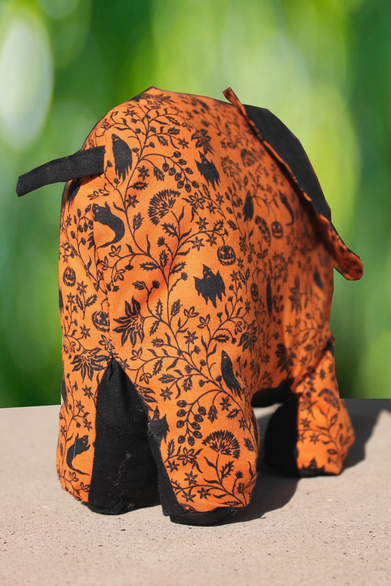 May include: Orange and black Halloween-themed fabric elephant with a black floral pattern. The elephant is standing on a light brown surface.