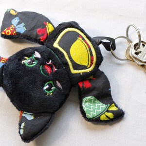 May include: Black plush bat keychain with colorful fabric wings and a yellow lemon design. The keychain has a black strap and a silver key ring with keys attached.