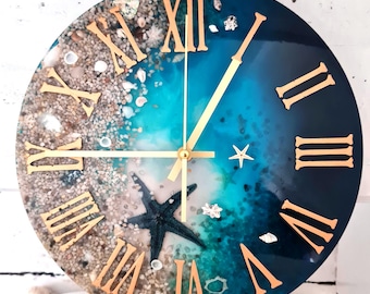 May include: A round blue and white resin clock with gold Roman numeral markings and gold hands. The clock face features a design of sand, seashells, and a starfish.